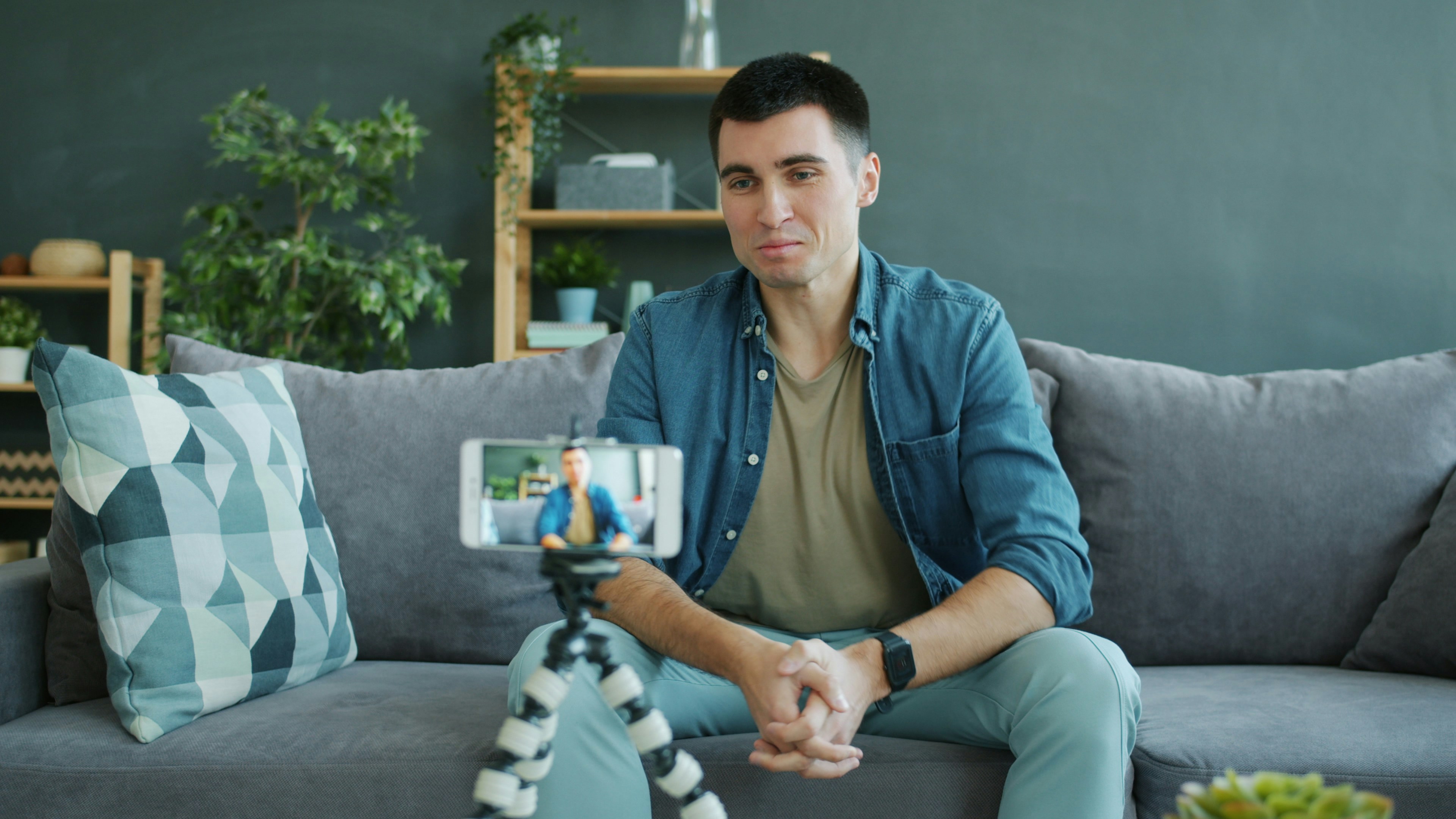 Man recording a video on his phone while seated on a couch